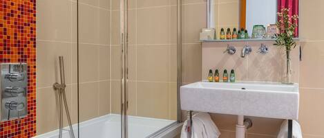 Un baño moderno con ducha envuelta en vidrio, un lavabo blanco con artículos de aseo y un espejo sobre el lavabo.