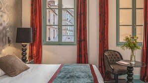 A hotel room with a bed, a chair, a table with a vase, and a window with curtains. - Hotel Le Petit Paris (Paris)
