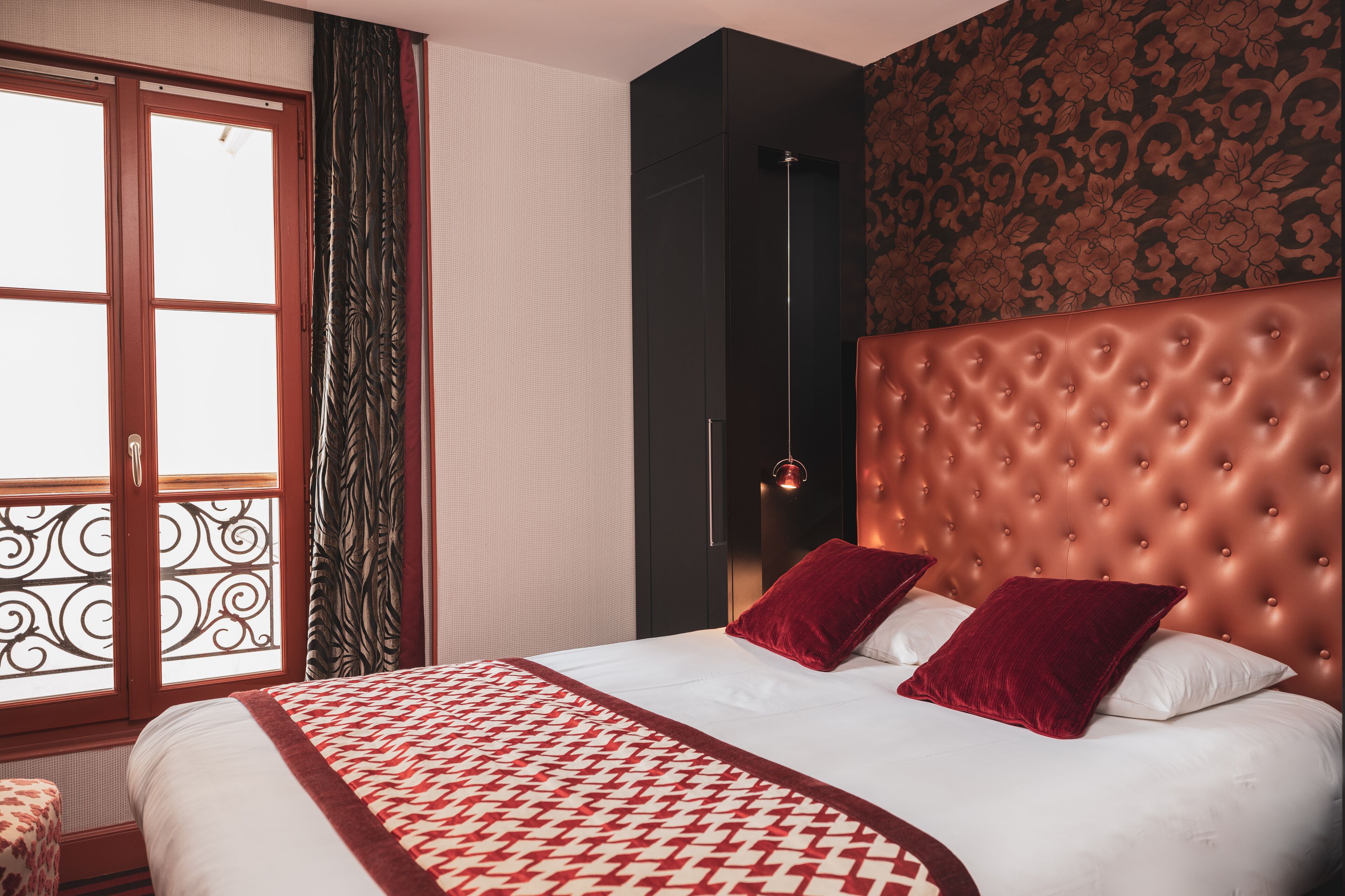 A hotel room with a large bed, a window with curtains, and a patterned wall.