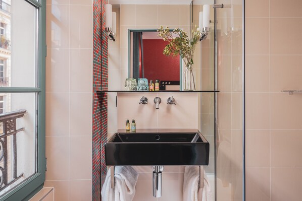 Un baño con un lavamanos negro, un espejo encima y una ventana a la izquierda.