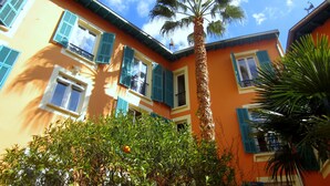 A building with a palm tree in front, a balcony, and a window with a shutter. - Maison Durante (Nice)