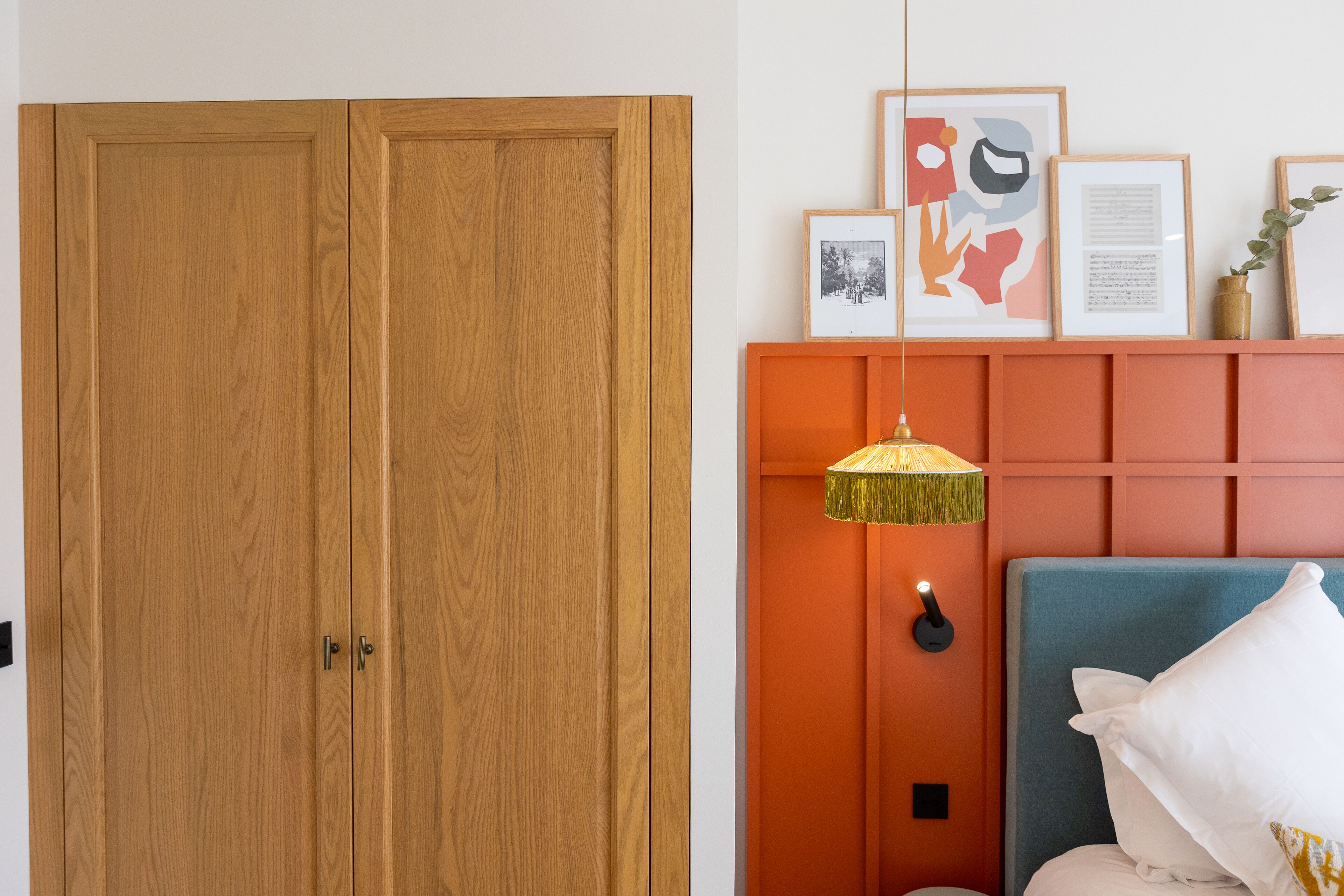 A bedroom with a wooden wardrobe, a bed with a blue headboard, and framed artwork on the wall.