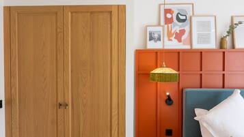 A bedroom with a wooden wardrobe, a bed with a blue headboard, and framed artwork on the wall.