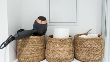 Drie gevlochten manden op een plank, waarvan er één een haardroger bevat en de andere een opgerolde handdoek.