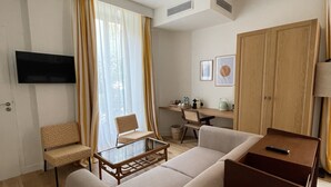 A modern living room with a sofa, armchair, and a small coffee table. There is a TV mounted on the wall, a wooden wardrobe, and a desk with a chair. - Maison Durante (Nice)