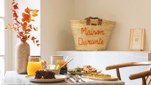 A breakfast table with a vase of leaves, a bottle, a glass of orange juice, a plate of food, and a basket labeled "Maison Durantte". - Maison Durante (Nice)