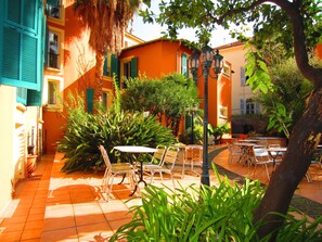 A courtyard with outdoor seating, a street lamp, and a building with orange walls and green shutters. - Maison Durante (Nice)