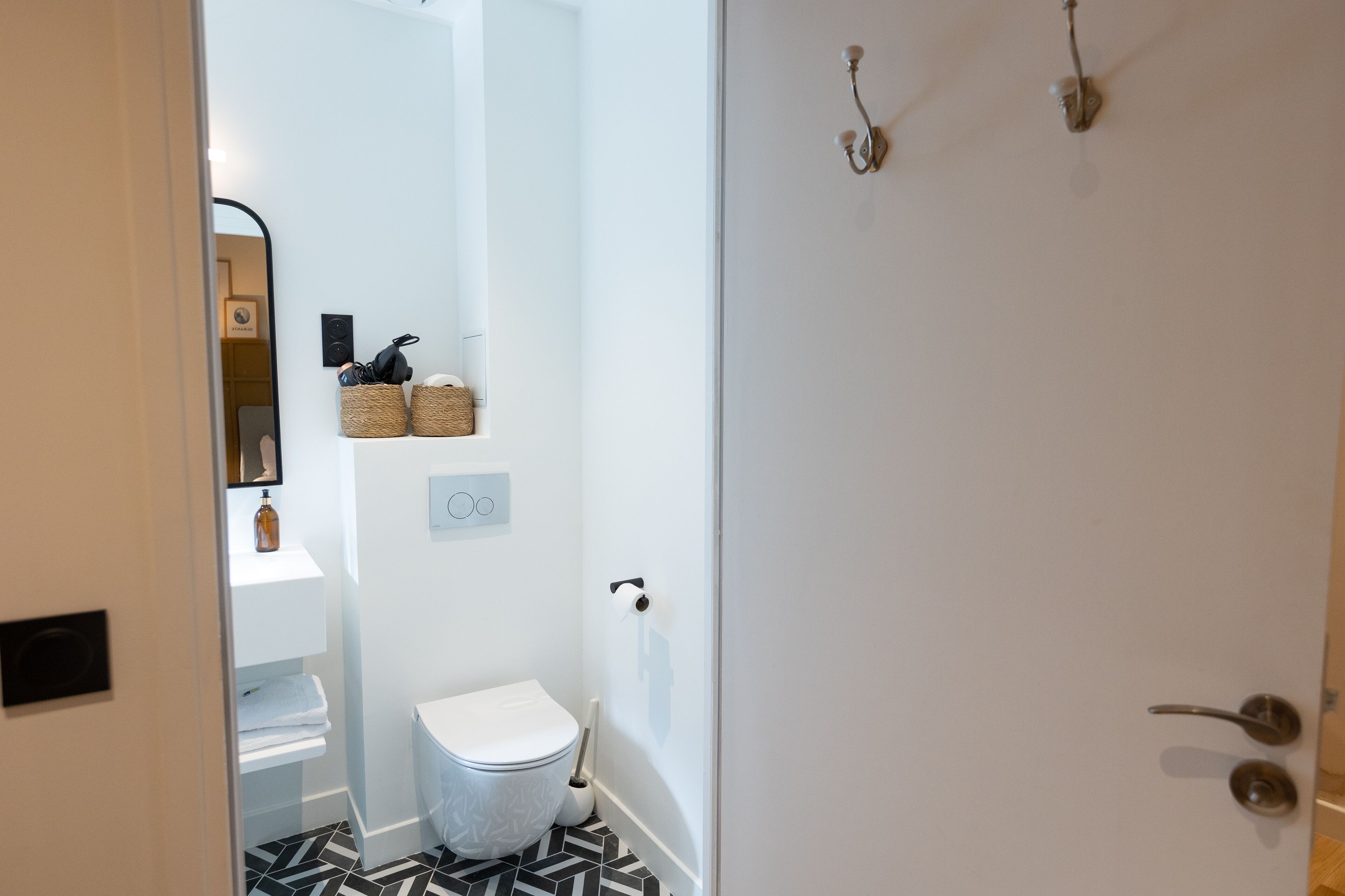 A bathroom with a white toilet, black and white patterned floor, and a mirror on the wall.