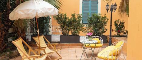 A patio with two wooden chairs, a white umbrella, and a metal table with yellow cushions.