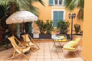 Une terrasse avec deux chaises en bois, un parasol blanc et une table en métal agrémentée de coussins jaunes.