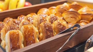 A wooden tray filled with glazed pastries, likely croissants, and a metal serving spoon.