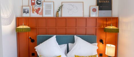 Ein Hotelzimmer mit Bett, zwei Nachttischlampen, einem Kopfteil und gerahmten Bildern an der Wand.