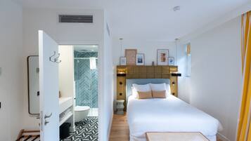 Habitación de hotel con cama, una mesita, baño con ducha y un pasillo con puerta.