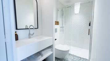 A modern bathroom with a white sink, mirror, and glass-enclosed shower.