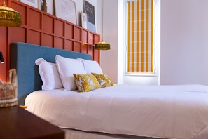 Un lit bien fait, avec des oreillers blancs et jaunes, une tête de lit bleue et un mur rouge orné de tableaux encadrés.