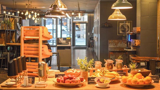 A breakfast buffet with various fruits and breads, wooden furniture, and hanging pendant lights. - Novotel Liverpool Centre (Liverpool)