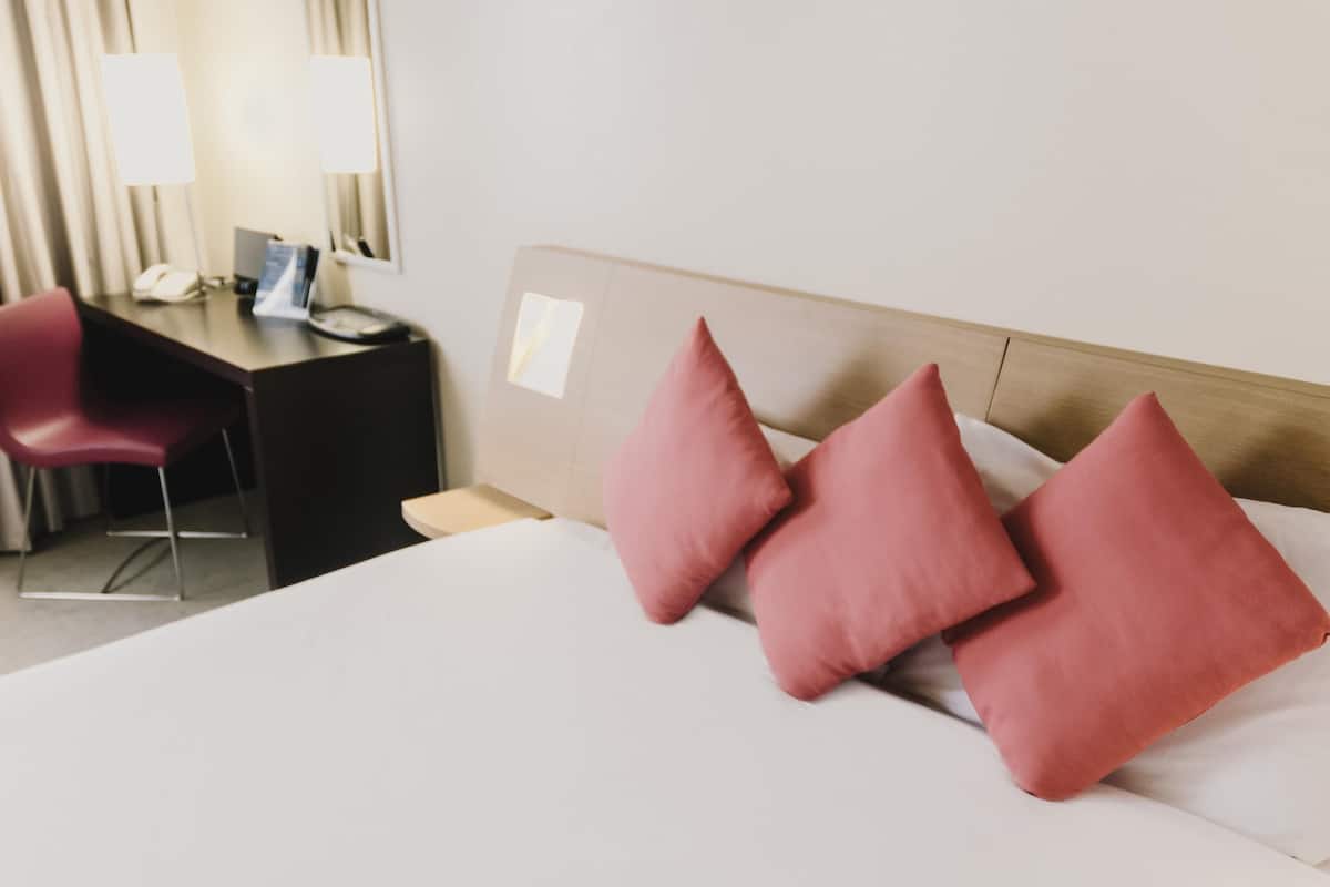 Ett hotellrum med en säng, ett skrivbord, en stol och en spegel.