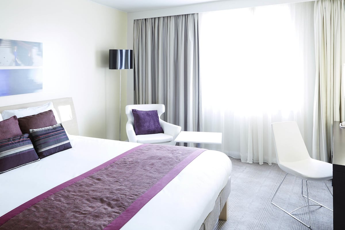 Ett hotellrum med en stor säng, en stol, ett skrivbord och en tv.
