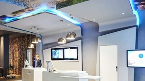 A modern hotel reception area with a reception desk, digital screens, and pendant lighting. - Novotel Liverpool Centre (Liverpool)