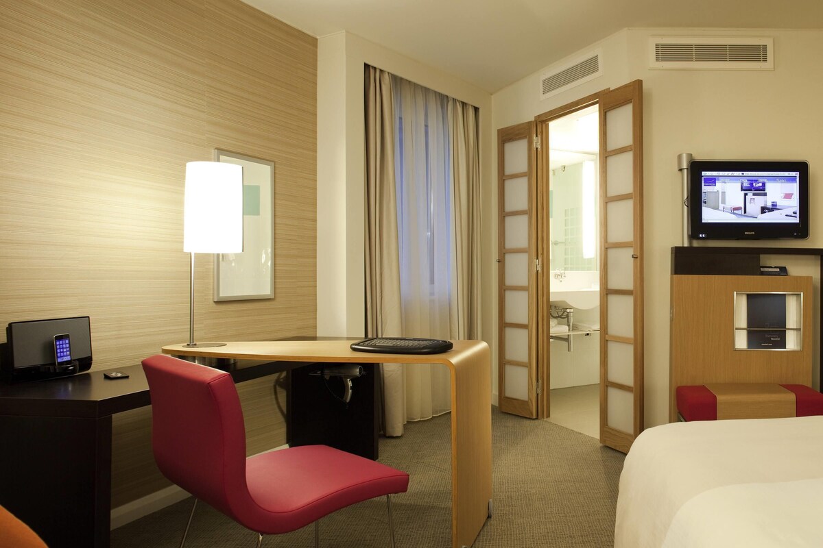 Ein Hotelzimmer mit Schreibtisch, Stuhl, Bett, Fernseher und einem durchgegangenen Tür einsehbaren Badezimmer.