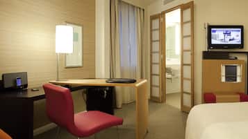 A hotel room with a desk, a chair, a bed, a television, and a bathroom visible through an open door.