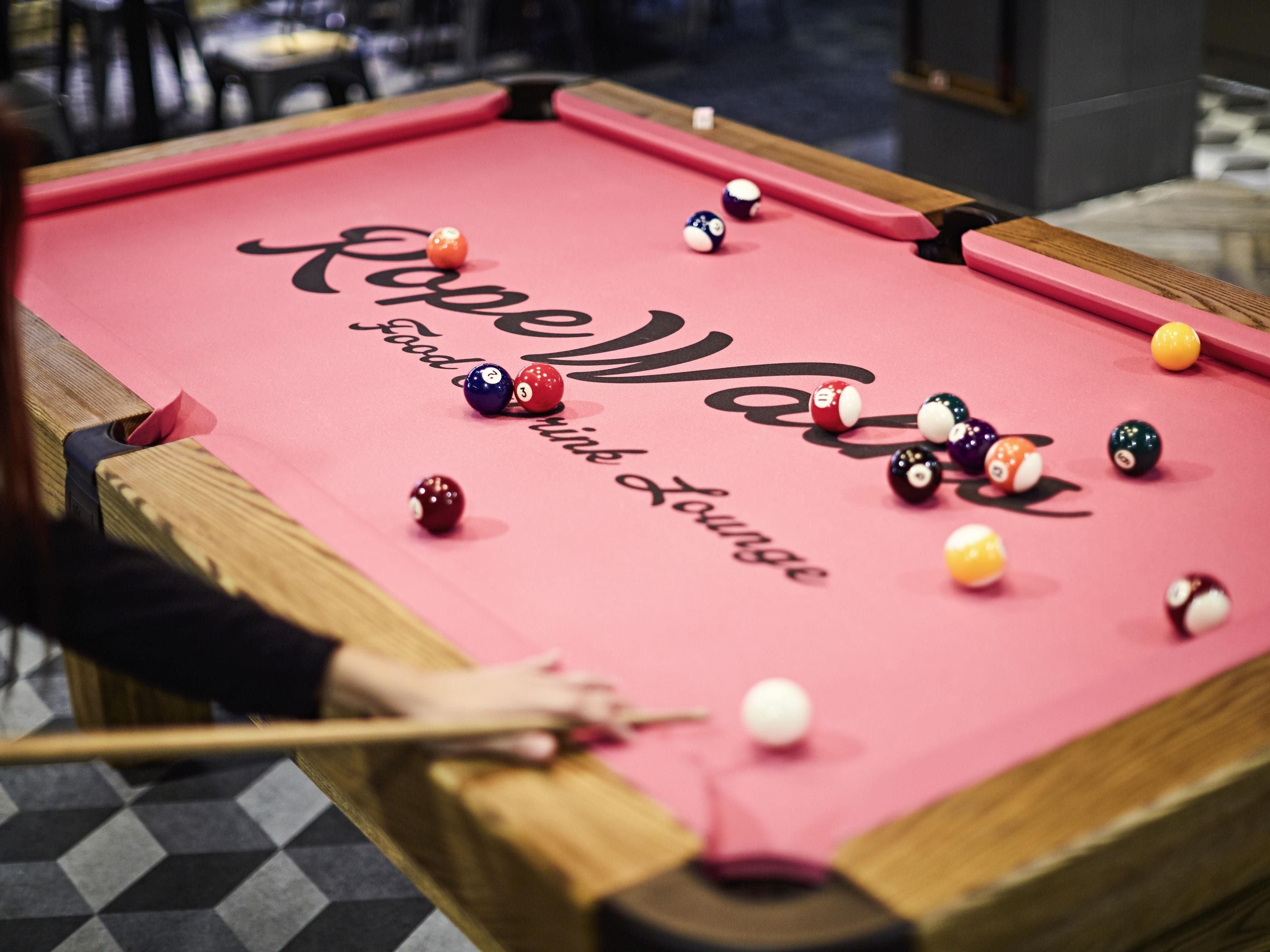Ein Billardtisch mit Kugeln und Spielstange, ein Holzkanten und ein Schachbrettmuster auf dem Boden.