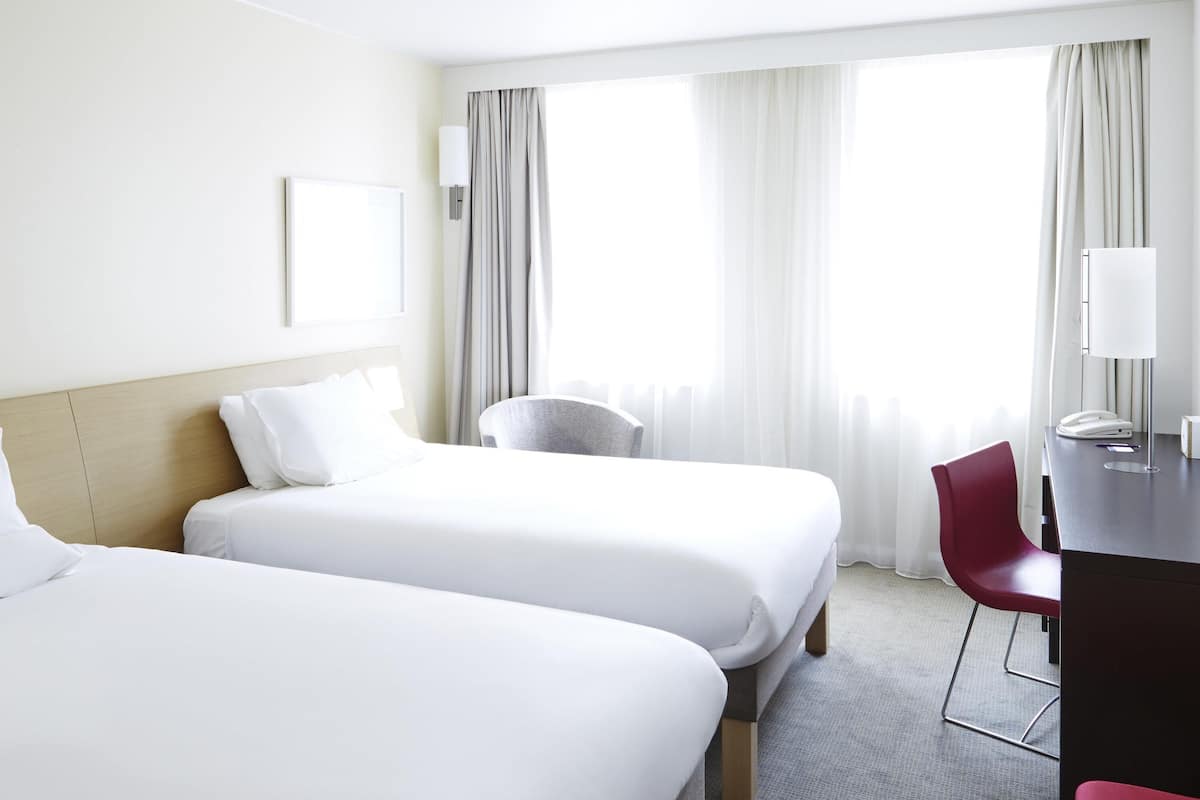 Ett hotellrum med två sängar, ett skrivbord, en stol och ett fönster med gardiner.