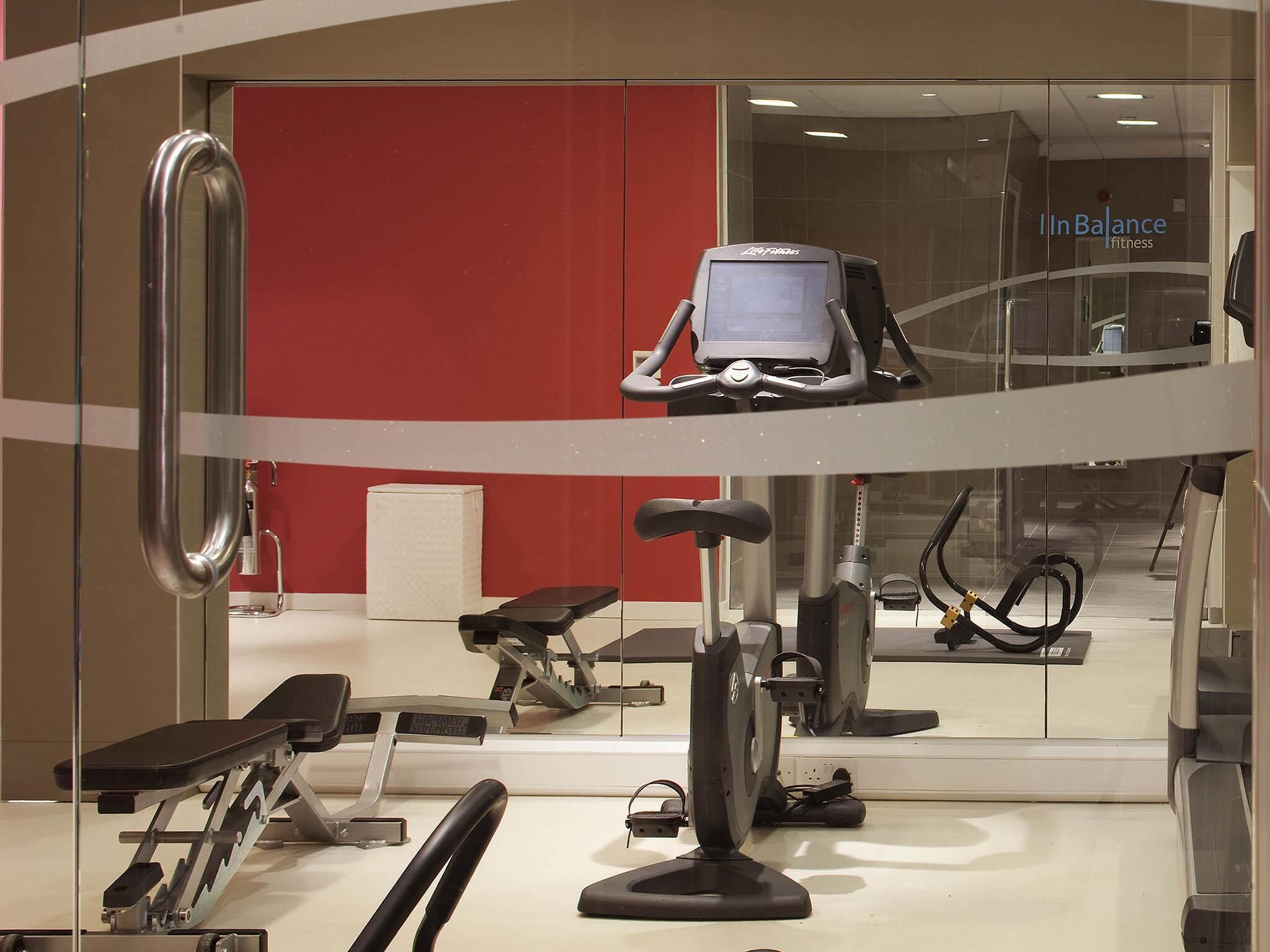 A gym with exercise equipment, a red wall, and a mirrored wall reflecting the equipment.