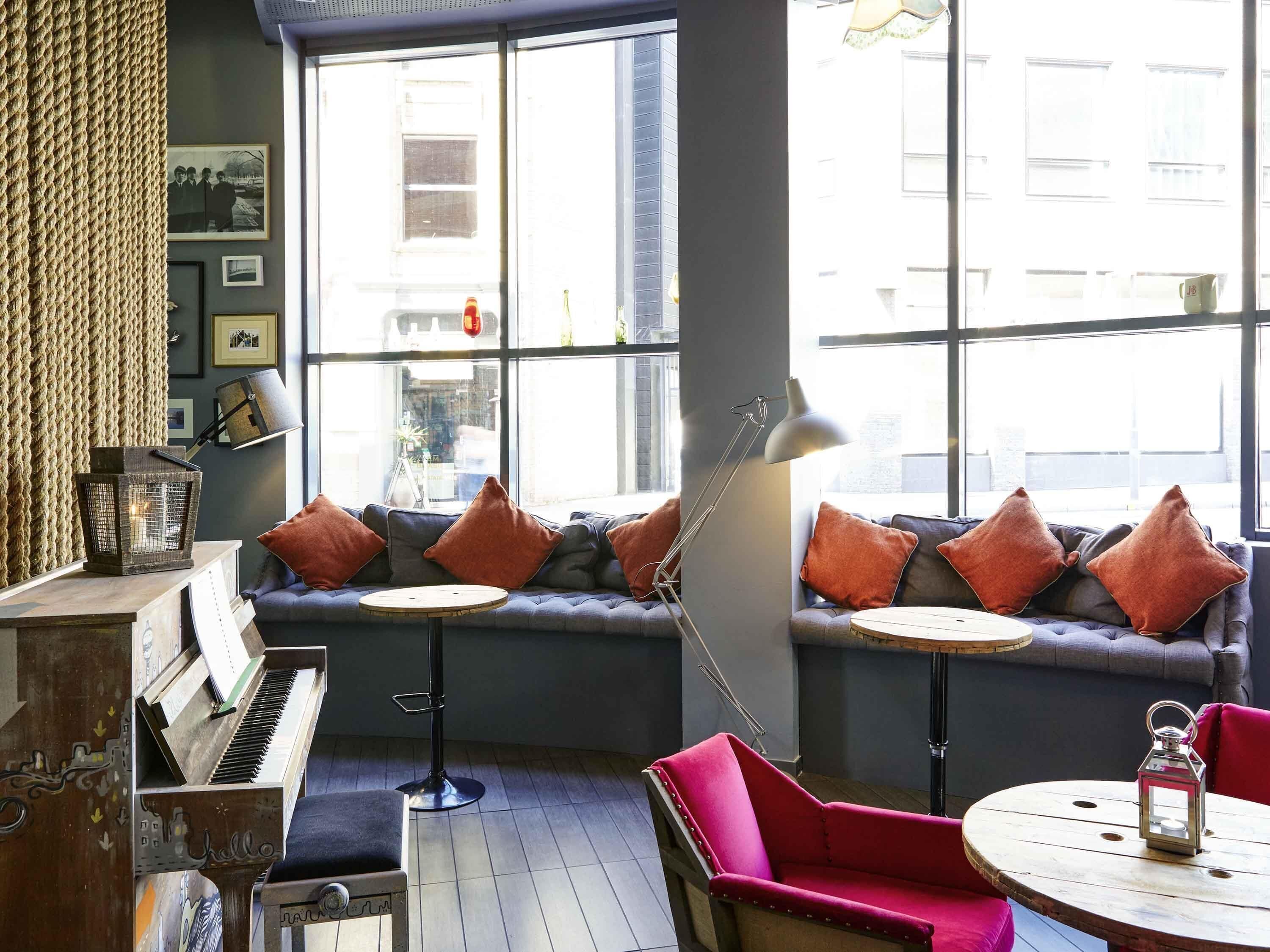 A cozy room with a piano, a bench, a red chair, a round table, and a bench with orange cushions.