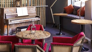 A cozy lounge area with a piano, red upholstered chairs, round wooden tables, and a sofa with cushions. - Novotel Liverpool Centre (Liverpool)