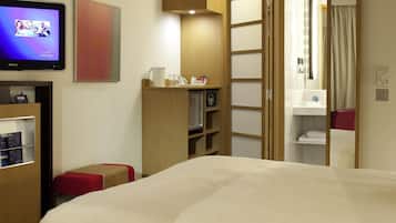 Habitación de hotel con cama, televisor, aparador de madera, una pequeña mesa con jarrón y baño visible a través de una puerta abierta.
