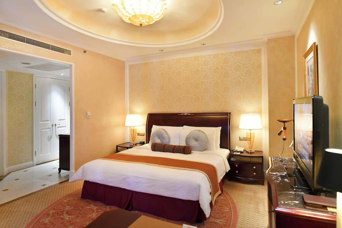 A hotel room with a large bed, two bedside tables with lamps, a television, and a door leading to another room.