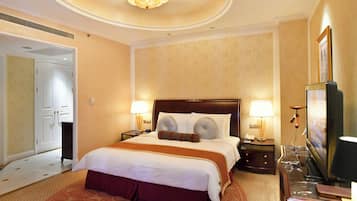 A hotel room with a large bed, two bedside tables with lamps, a television, and a door leading to another room.
