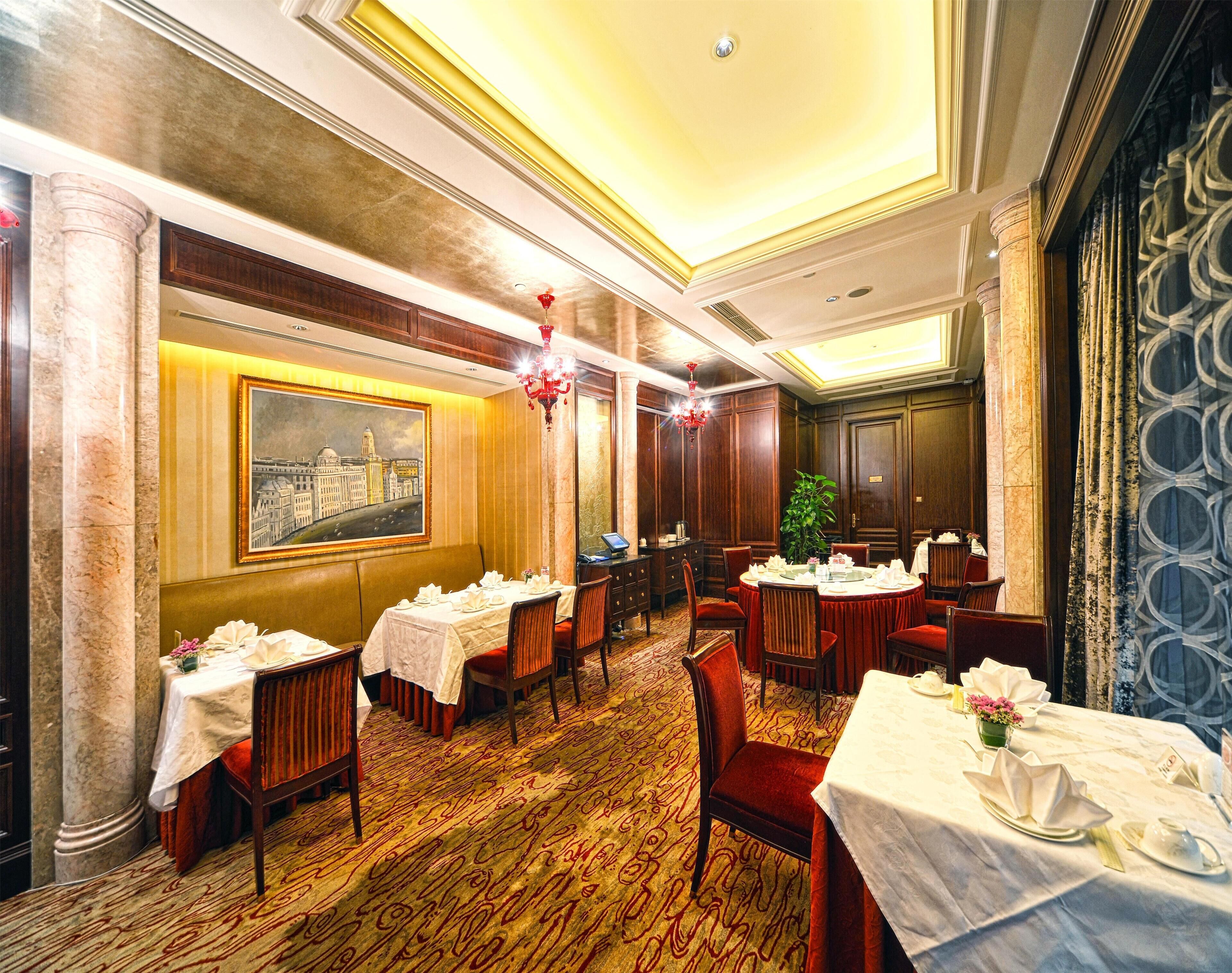 A hotel dining room with round tables, red chairs, and a large painting on the wall.