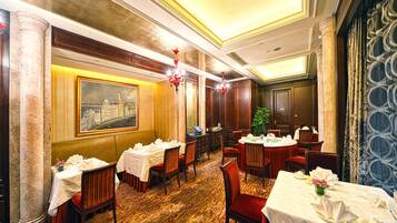 A hotel dining room with round tables, red chairs, and a large painting on the wall.