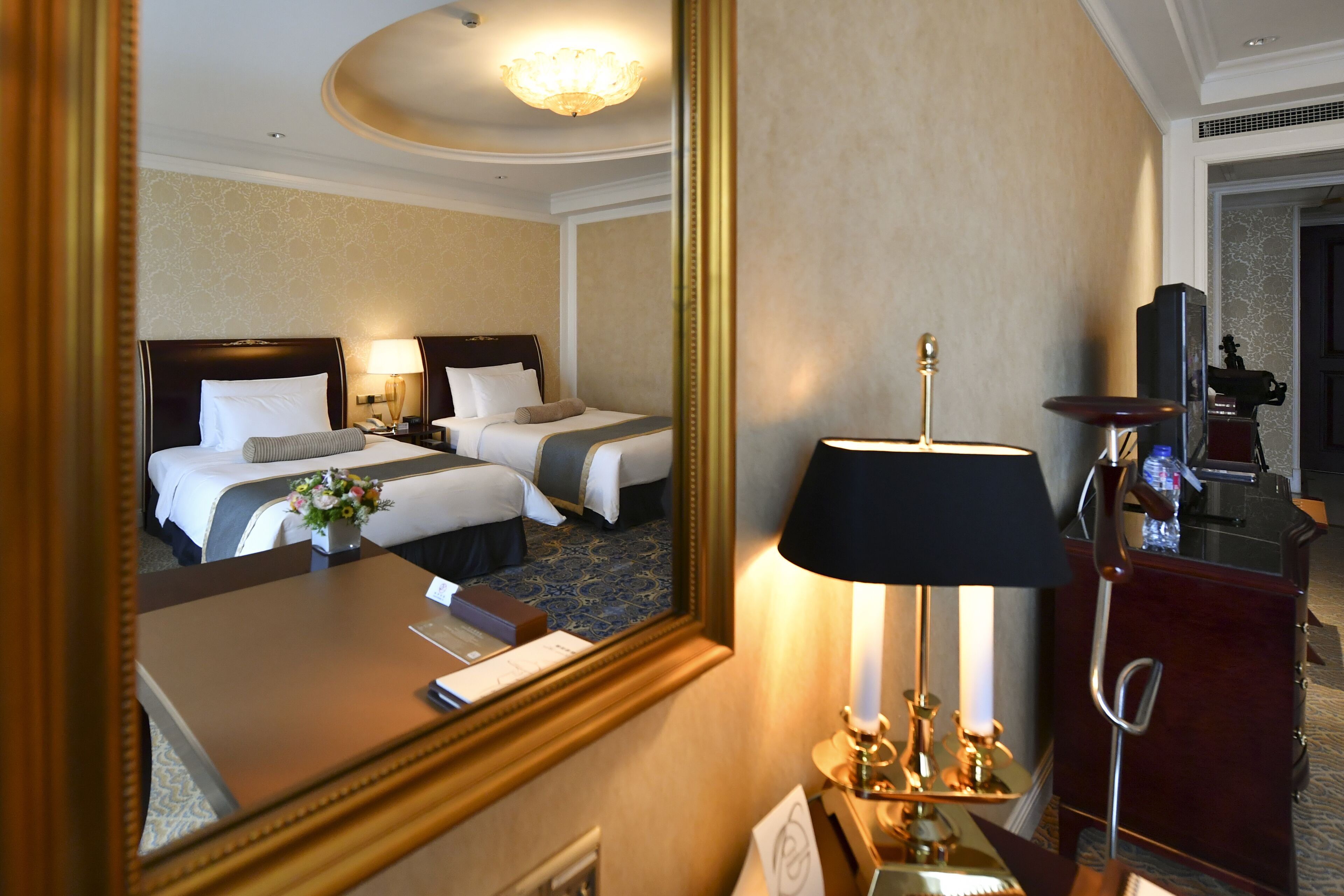 A hotel room with two beds, a desk, a mirror, a lamp, and a dresser.