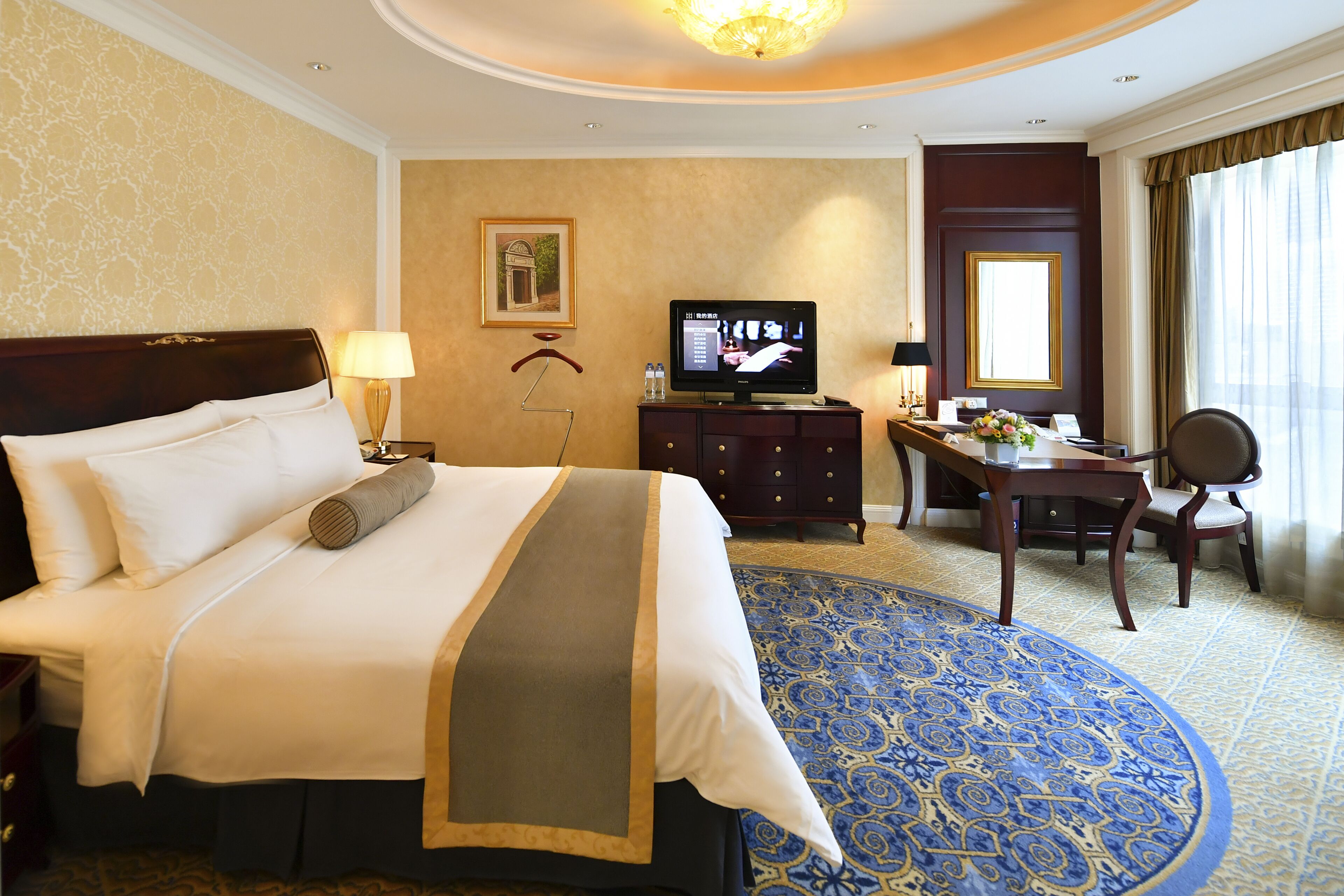 Une chambre d’hôtel avec un grand lit, un bureau avec une chaise, une télévision et un tapis décoratif.