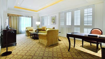 A hotel room with a patterned carpet, a sofa, a chair, a desk, and a lamp.