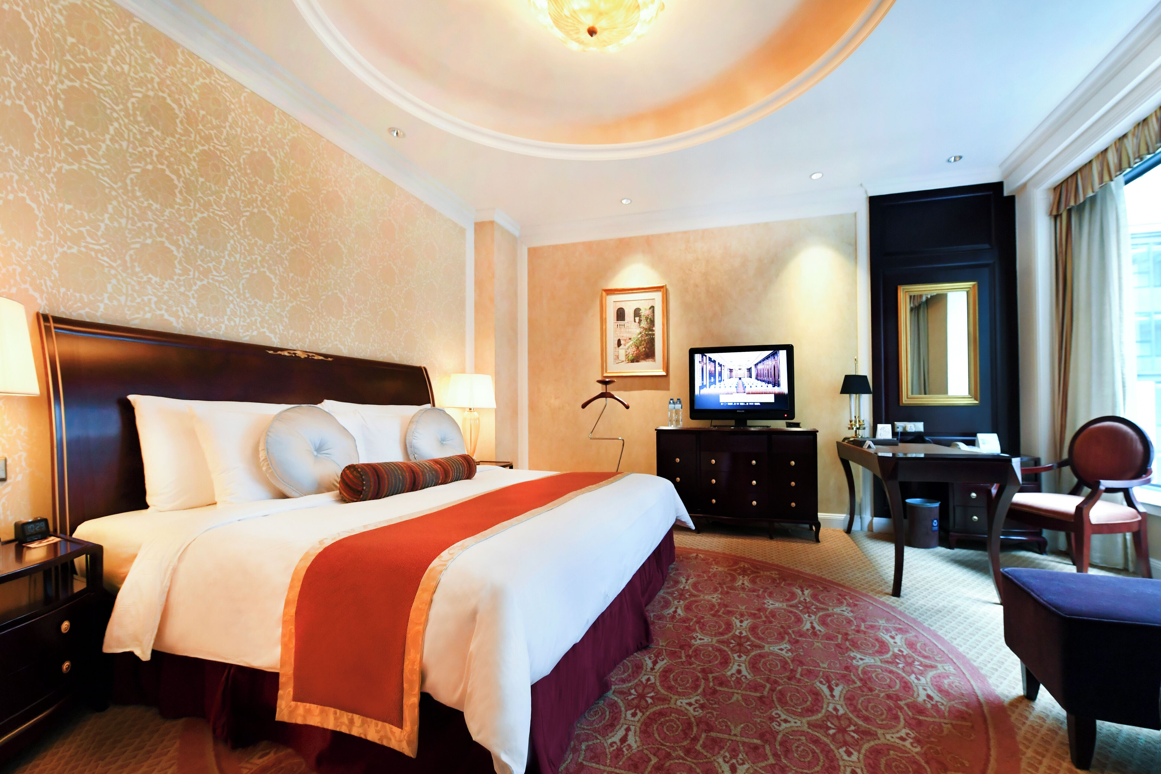A hotel room with a large bed, a desk, a television, and a chair.