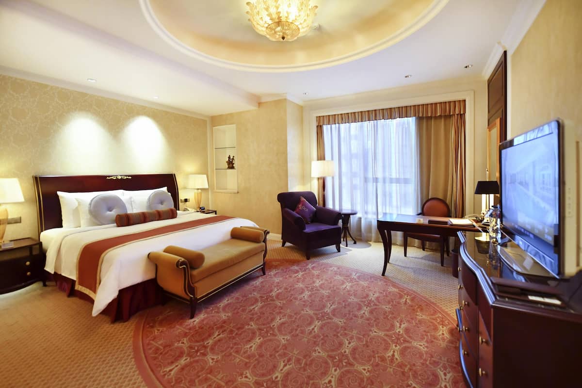 A hotel room with a large bed, a desk, a chair, a television, and a chandelier.