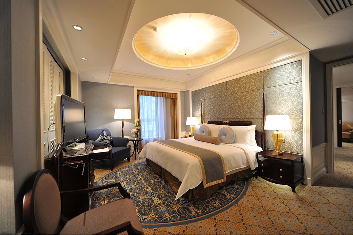 A hotel room with a large bed, a desk with a chair, a television, and a carpeted floor.