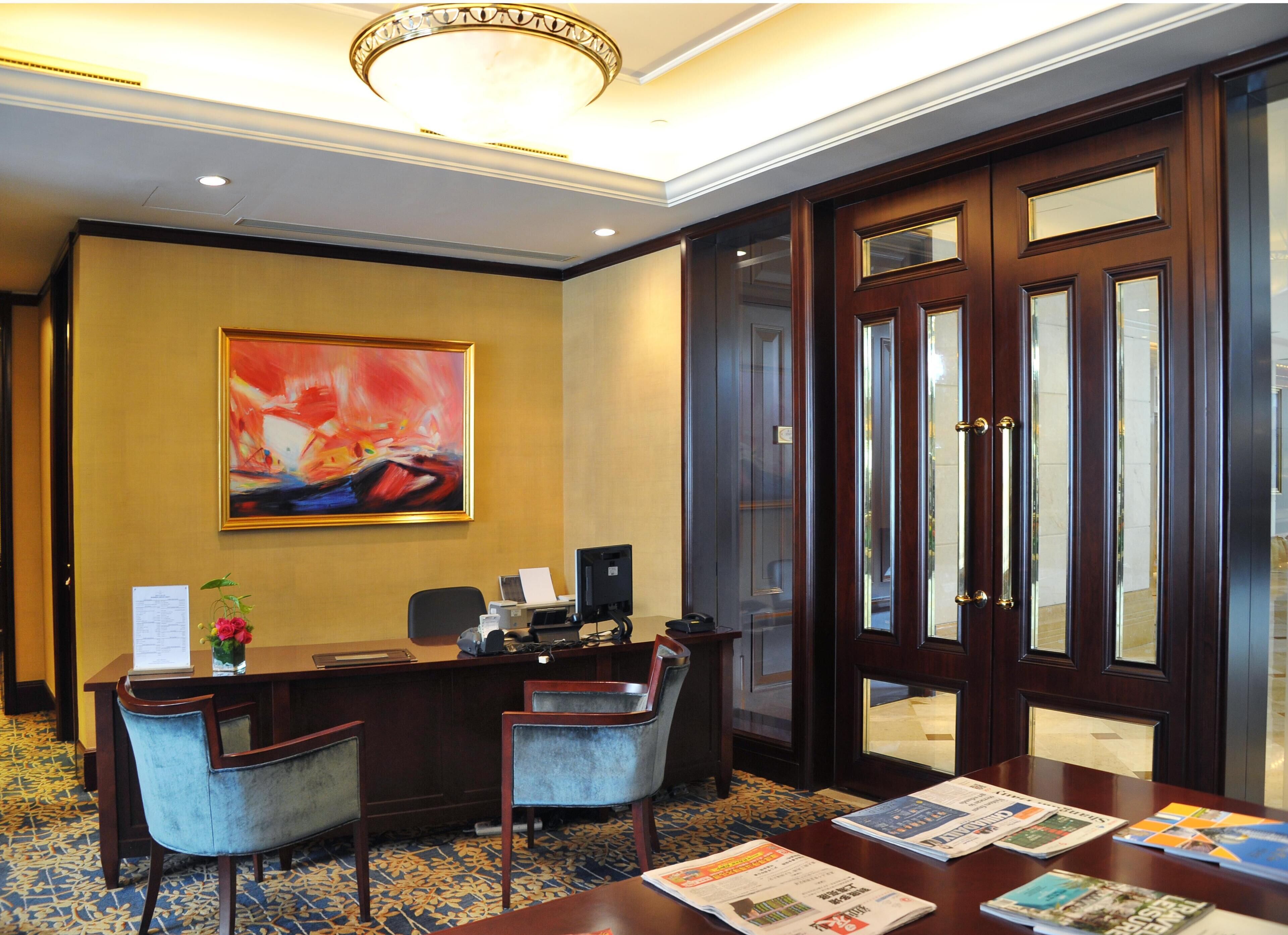 A reception area with a desk, chairs, a large abstract painting, a computer, and a door with glass panels.