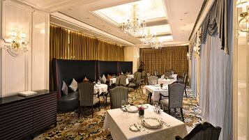 A formal dining room with tables set for service, elegant chandeliers, and a patterned carpet.