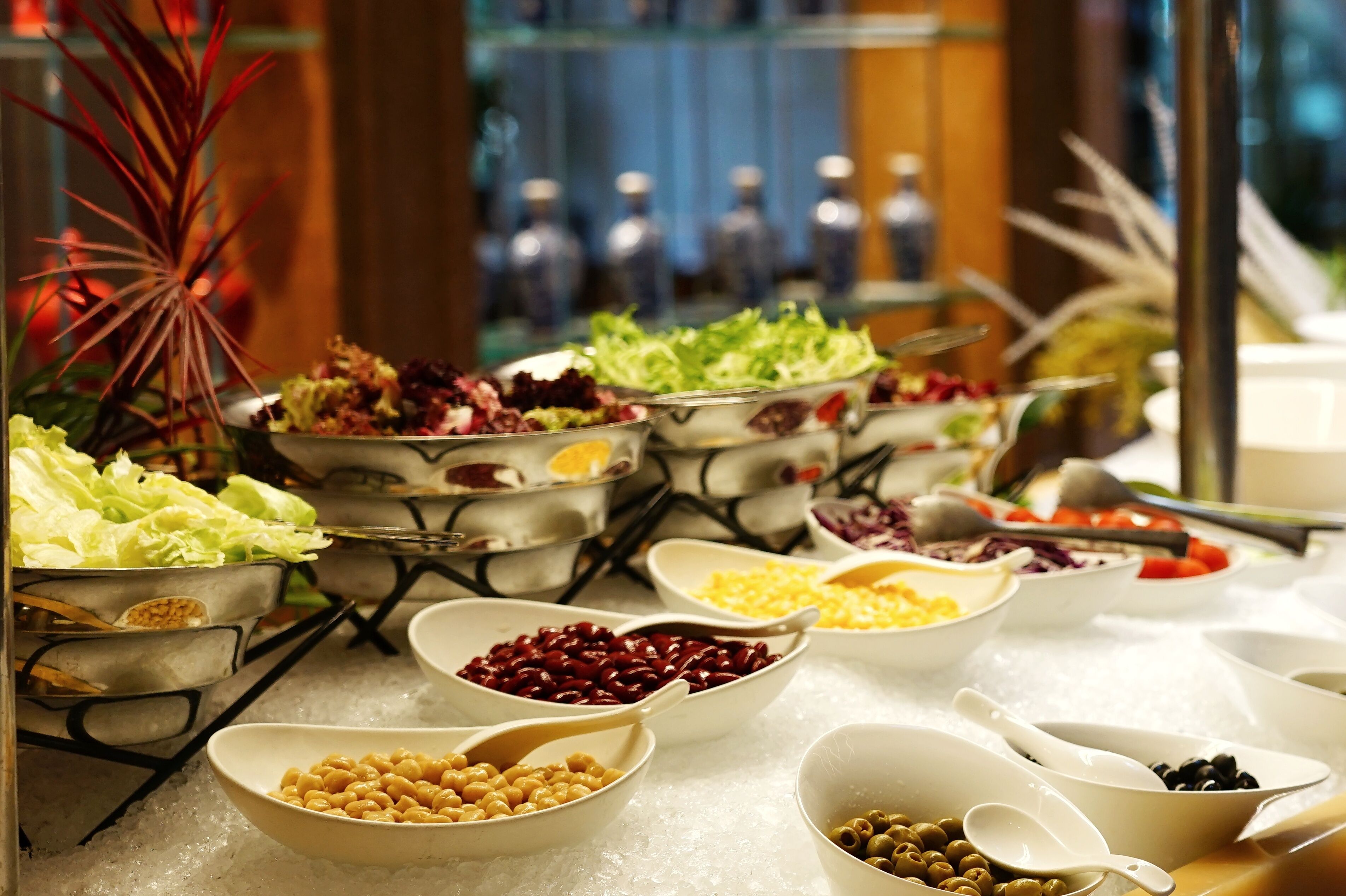 Une table de buffet avec différents plats présentés dans des bols et servis à l’aide de cuillères, le tout disposé sur une table recouverte d’une nappe blanche.
