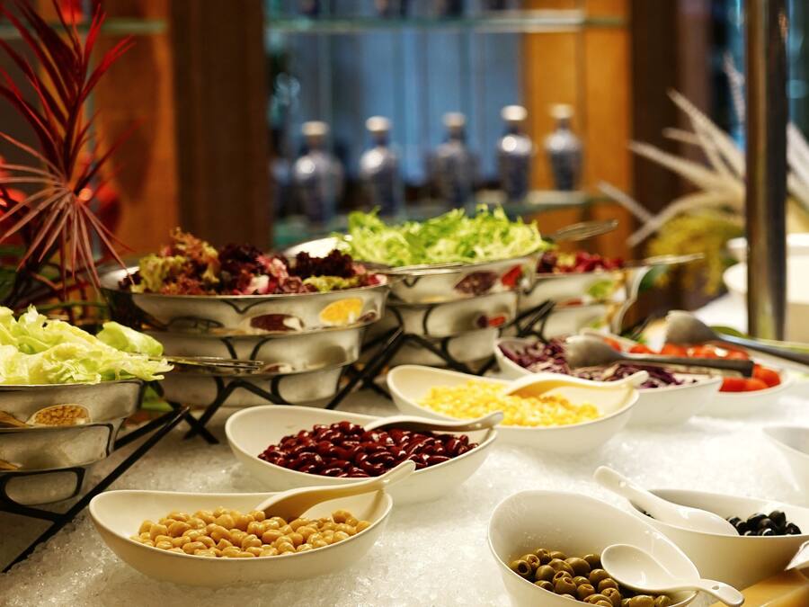 A buffet table with various food items in bowls and spoons, set on a table covered with a white cloth.