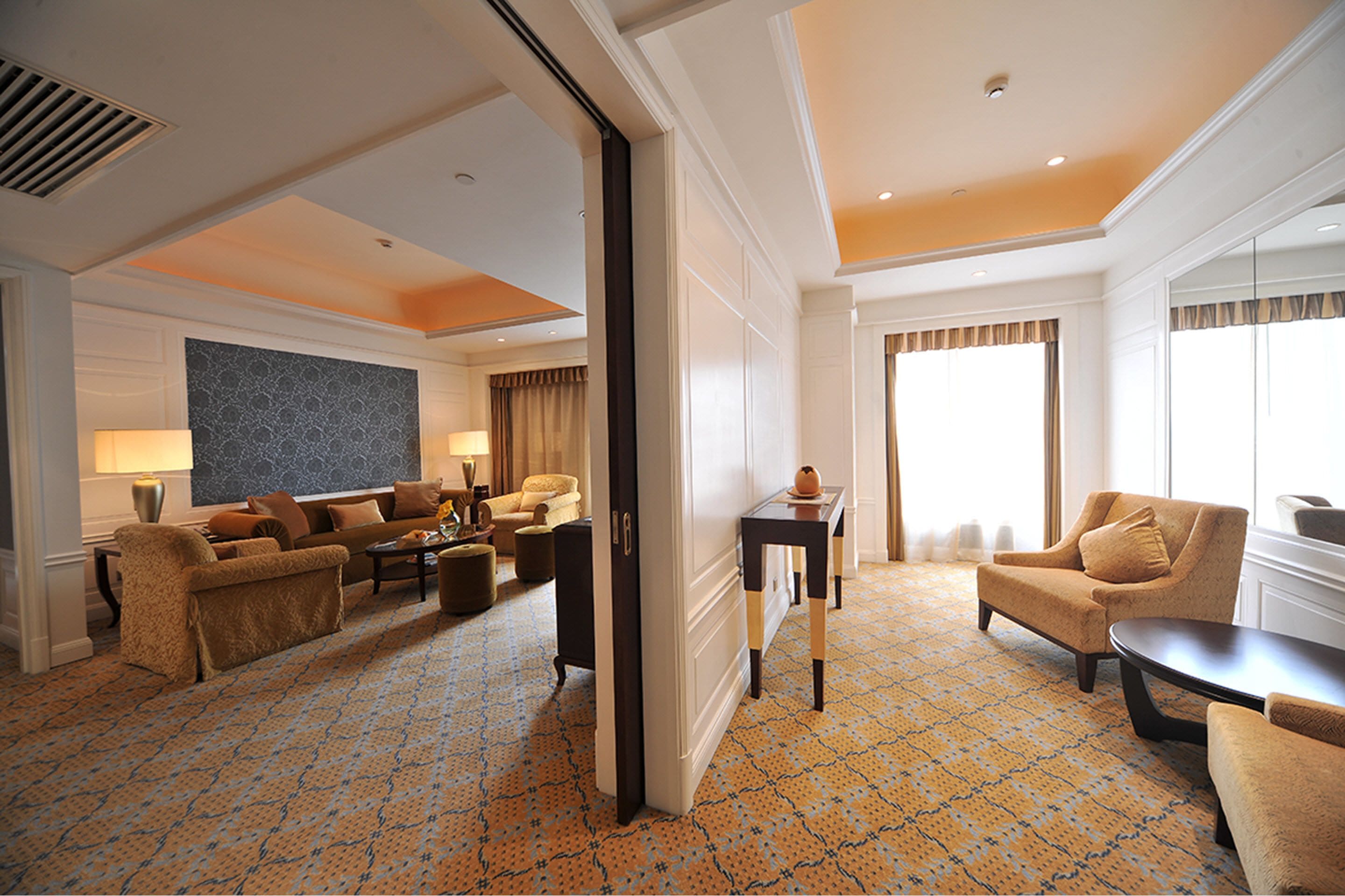 Une chambre d’hôtel spacieuse, dotée d’un tapis à motifs, d’un ensemble de canapés, d’une table basse et d’une grande fenêtre avec des rideaux.