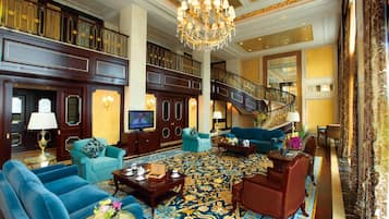 A spacious lobby with a grand staircase, multiple seating areas, and a large chandelier.