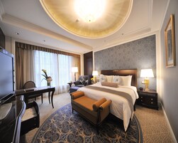A hotel room with a large bed, a desk, a chair, a TV, and a window with curtains.
