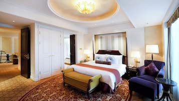 A hotel room with a large bed, a sitting area with a chair and ottoman, a small table, and a chandelier.