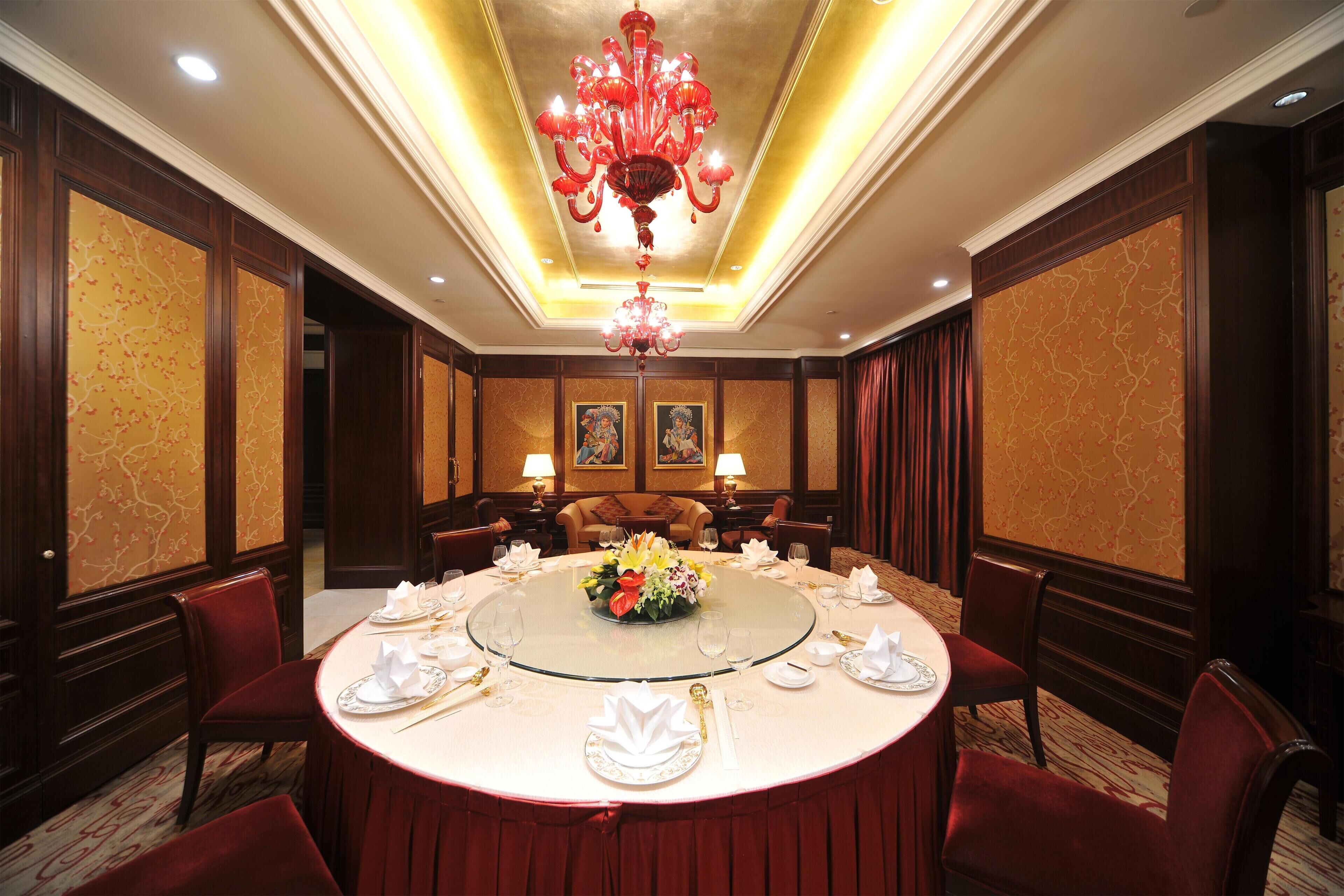A formal dining room with a round table, red upholstered chairs, and a chandelier.